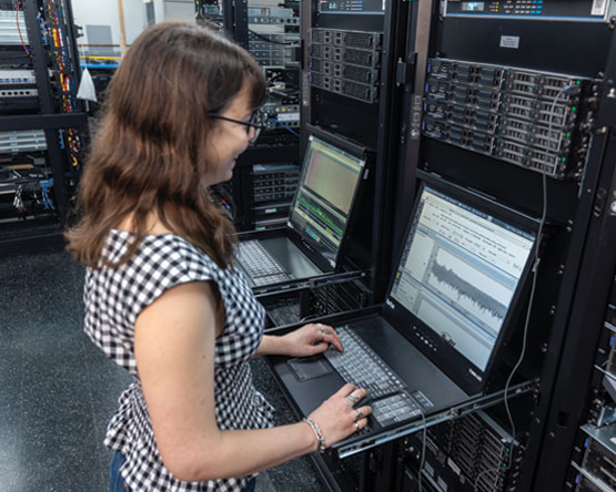 A women standing in front of a laptop, working on the signals shown on the screen.