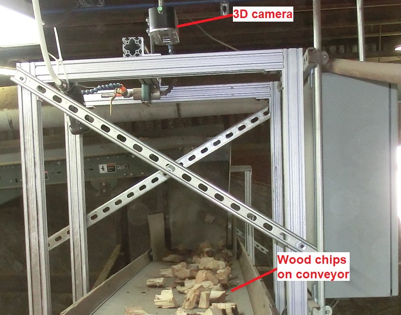 conveyor belt with wood chips laying on belt and a 3D camera mounted above the belt