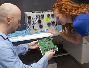 Two engineers in a lab reviewing a green circuit board