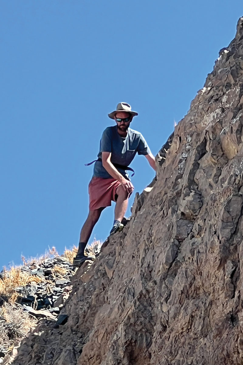 Dr. Adam Cawood examining faults in Clayton Valley, Nevada, perched on a rock formation on a clear sunny day