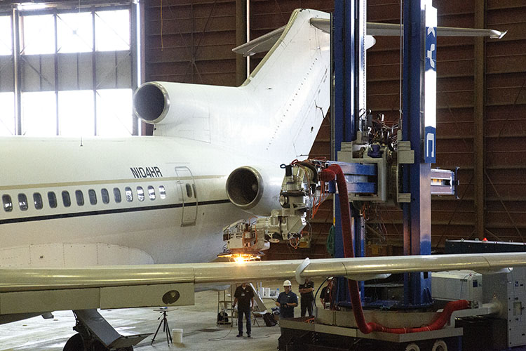 Aircraft in a hangar with a large robot removing paint from the wing with a laser