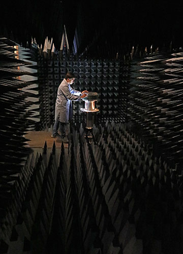 a dark anechoic chamber with a person in a lab coat placing an antenna in the room. 