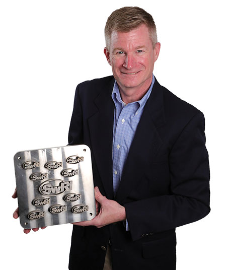 Carl Popelar holding a titanium block with the SwRI logo cut into it numerous times