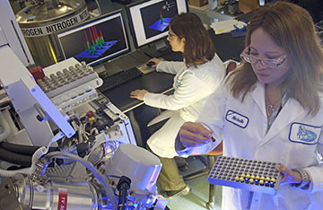 Two scientists in white coats inside a biology lab with equipment 