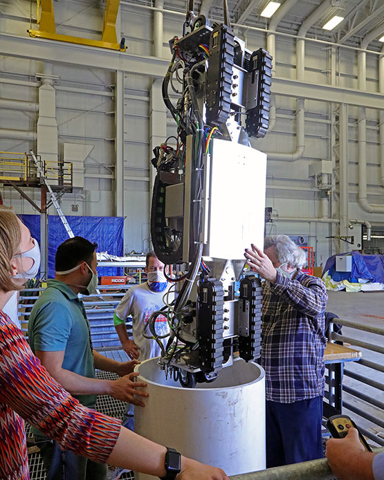 team members place a mobile robot into a tight cylinder