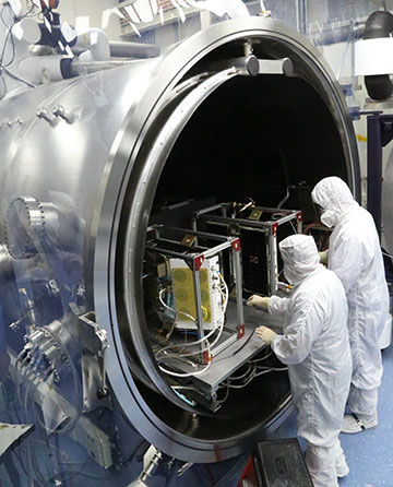 Two people in clean suits placing CYGNSS into a testing chamber