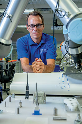 Portrait of Matt Robinson posed behind a robot arm