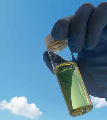 gloved hand holding a vial of fuel with a blue, clouded sky in the background