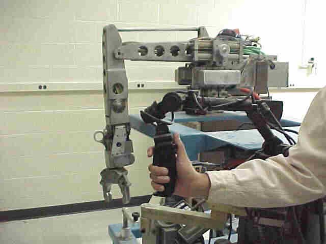 A man's hand, extended away from his body, controlling a robot using an encoder-based hand controller