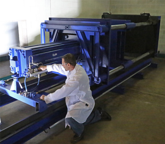 A person kneeling down to operate equipment that can crush test whole battery packs.