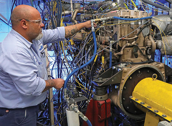 Technician in a blue shirt inspecting the diesel engine on a test stand