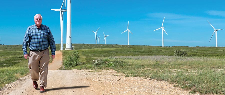 Gordon Wittmeyer walking down a dirt road with windmills in the distance