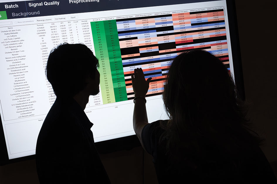 Two people cast in shadow against the backlight of a monitor screen that is showcasing Highlight, the software tool for chemical analyses.
