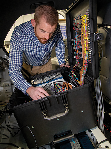 Senior Research Engineer Kevin Jones using a mobile data acquisition system inside of an electric vehicle.