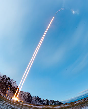 Orange light trails from rockets launching against a blue sky