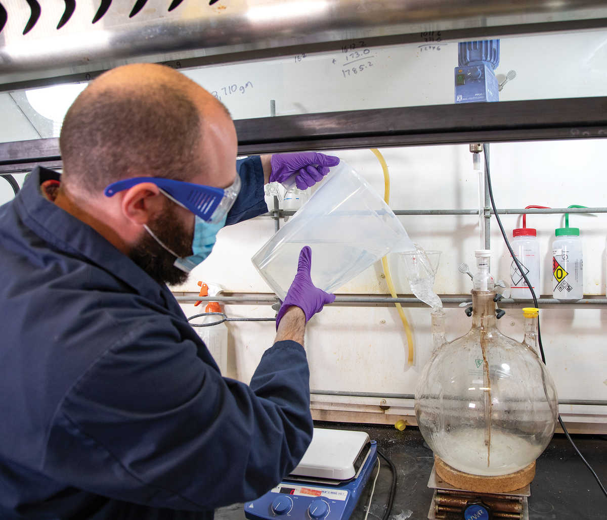 man in personal protective gear pouring chemicals into funnel