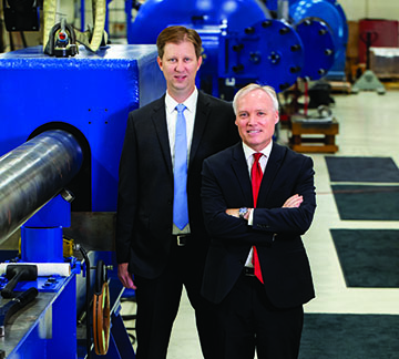 Dr. Nicholas Mueschke (left) and Dr. James Walker standing in front of blue machinery 