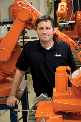 Portrait of Paul Evans standing among several orange robots