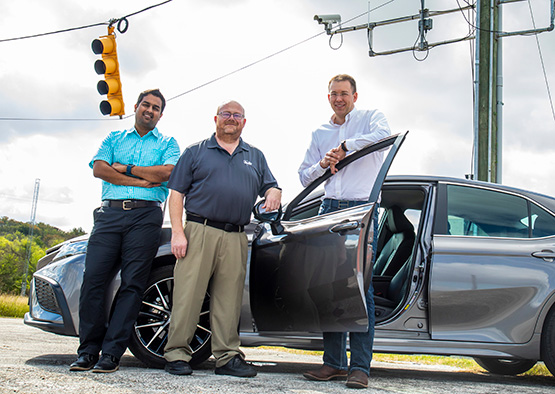 Sankar Rengarajan, Michael Brown and Scott Hotz posing in front of a car. 