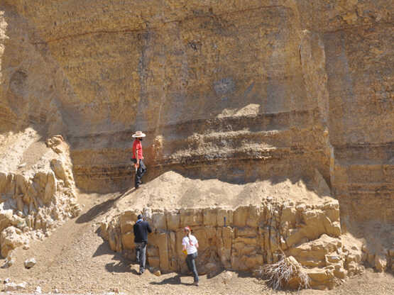 Three people in front of a carved basin wall with large fractures.