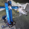 Blue robot comprised of two segments - the first is vertical with XYREC in white lettering; the second is horizontal to the ground with a laser attached. The robot is using a laser to remove an aircraft coating