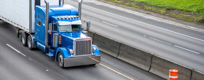 Classic big rig blue semi truck with high chrome exhaust pipes transporting cargo in refrigerator semi trailer running on the divided road