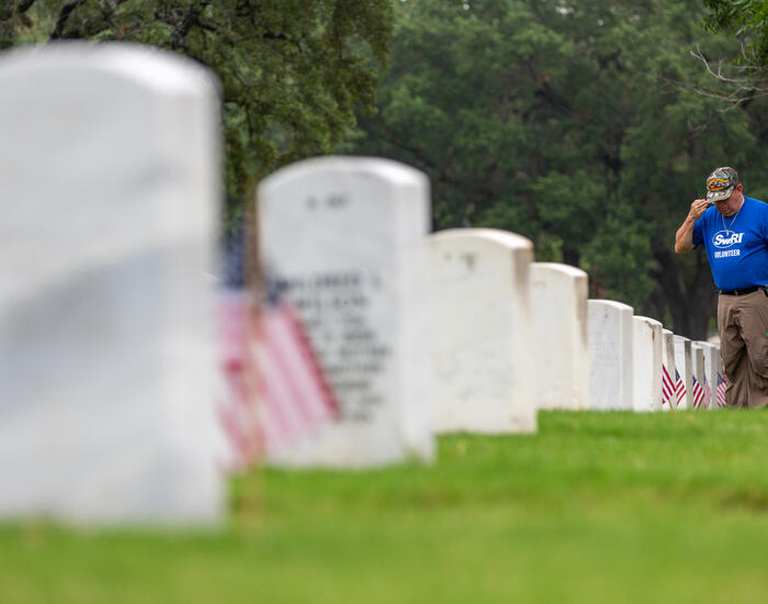 Looking down a row of tombstones with SwRI staff member in the distance placing a flag at a tombstone