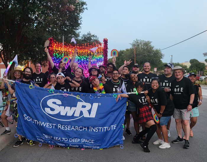 group of SwRI employees wears LOVE shirts holding a blue Southwest Research Institute banner