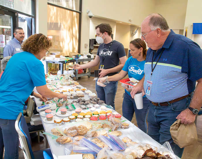 woman in blue shirt arranging baked goods as 2 men and a woman make purchases