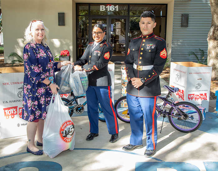 female SwRI employee handing back of toys to 2 USMC soldiers