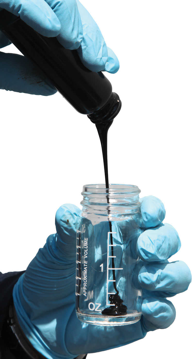 blue gloved hands pouring crude oil into a clear jar