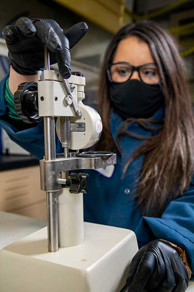 masked woman in blue lab coat performing hardness measurements with durometer