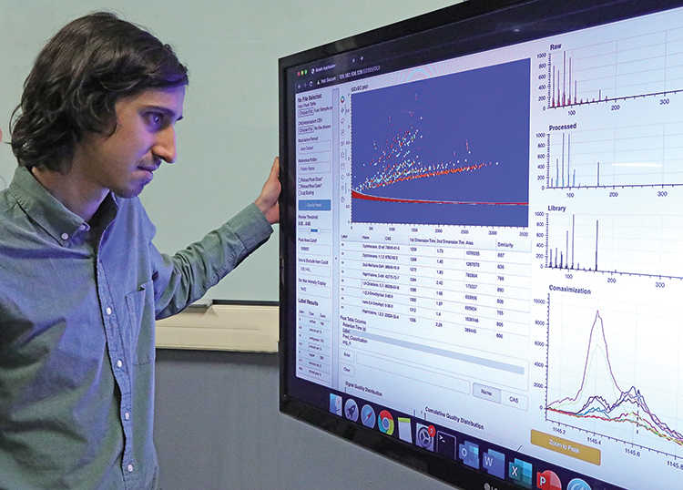 man standing in front of large computer monitor with left hand holding edge looking at floodlight software