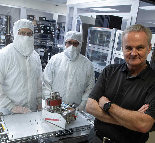 two men in cleanroom suits standing behind maps tool with Dr. Jörg-Micha Jahn standing outside the room
