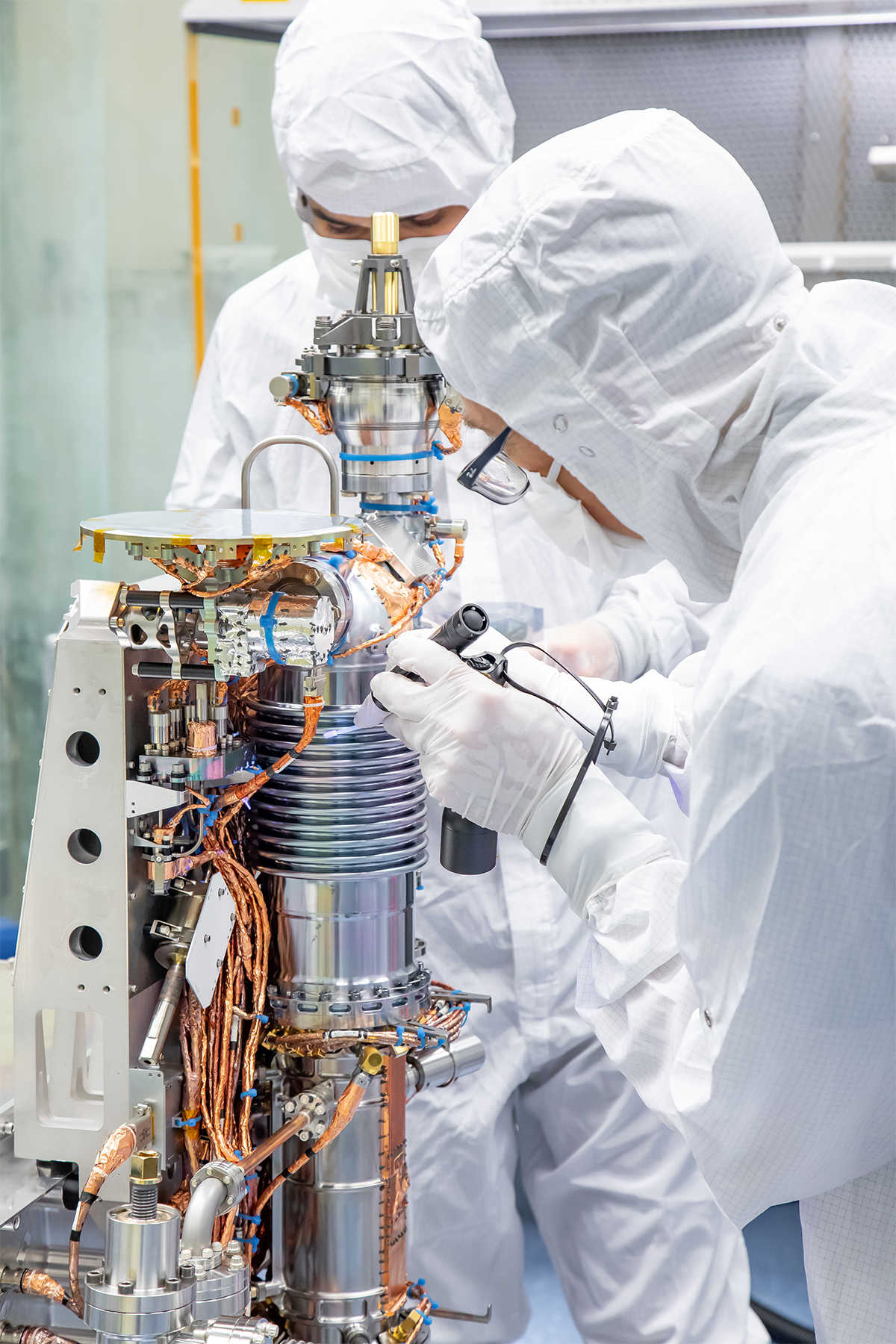 Two individuals in protective suits working on the mass spectrometer