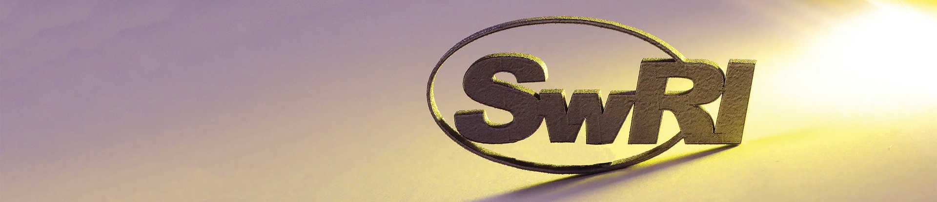 SwRI logo cut from a titanium block with a shadow falling on the left side