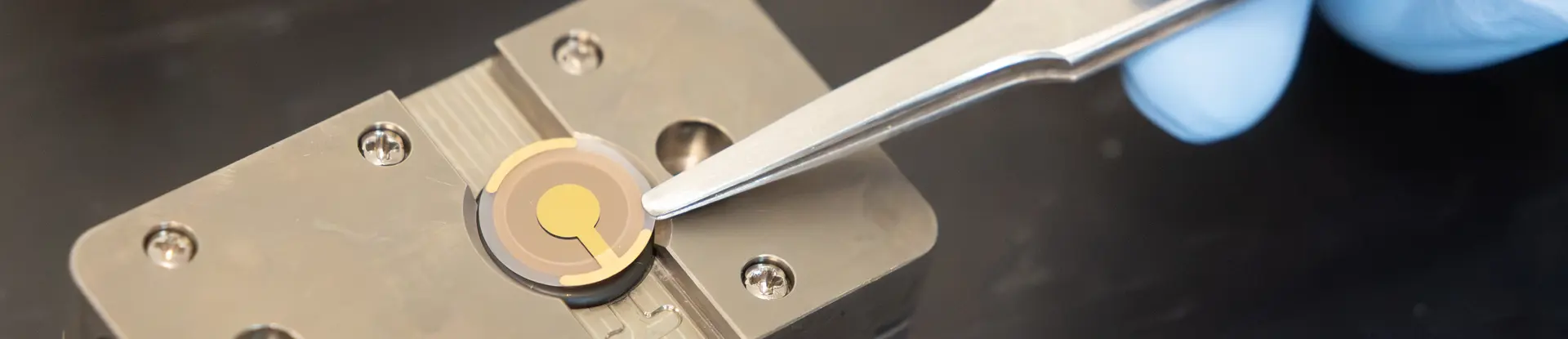 Closeup of a hand holding tweezers touching a biosensor