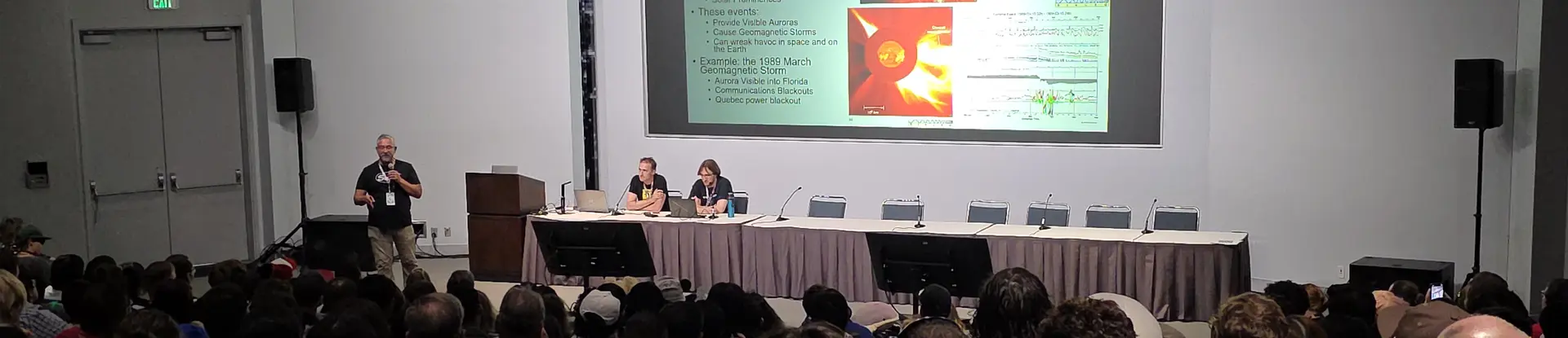 Photo of audience at San Japan gaming convention with the presentation of "Physics of Anime" on screen and Dr. Roman Gomez leading the discussion