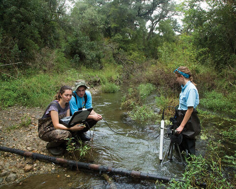 Three SwRI engineers water sampling at a river