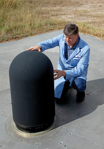 man in blue lab coat kneeling next to antenna installed on concrete pad