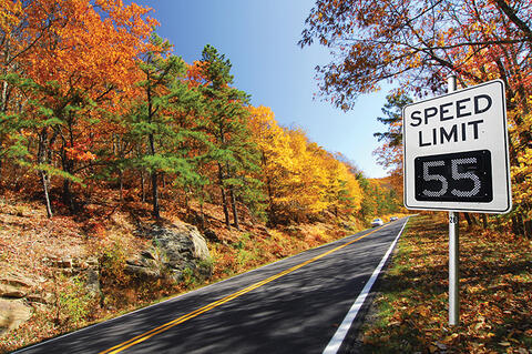cars in background driving toward a variable speed limit sign that reads 55 MPH