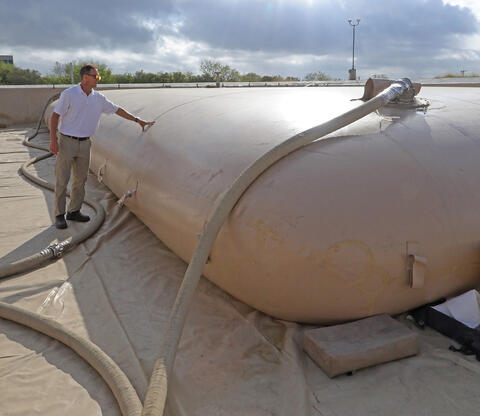 man standing adjacent with his hand on a large collapsible container used to supply fuel to tactical vehicles