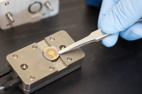 Closeup of a hand holding tweezers touching a biosensor