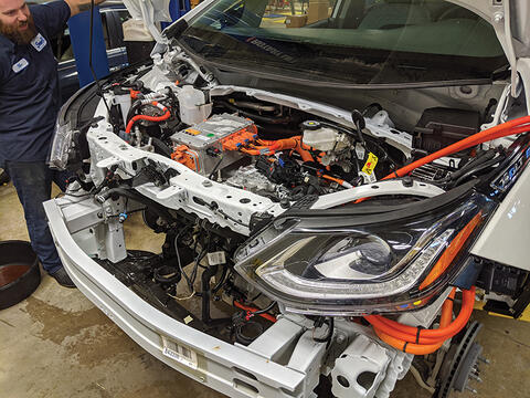 bearded white man in blue SwRI work shirt looking at the engine of an electric vehicle