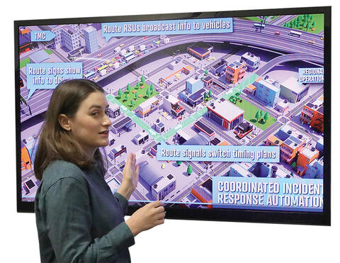 white woman standing in front of large television screen showing artist rendering of coordinated incident response automation