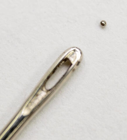 Microscopic projectile next to a sewing needle for size