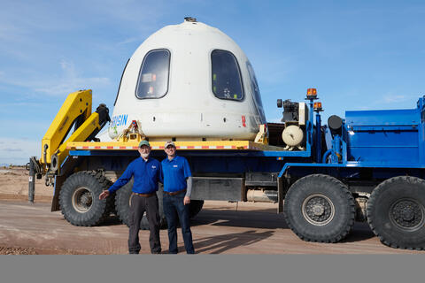 Engineer Kevin Supak and engineer Steven Green standing in front of part of Blue Origin’s New Shepard vehicle