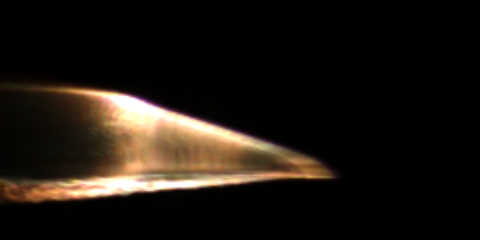 Conical projectile glowing yellow while in flight against a black background