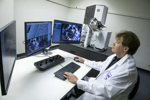 Engineer sitting at a computer desk viewing scanning electron microscope images