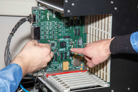 Two researcher's hands pointing to a part on a motherboard